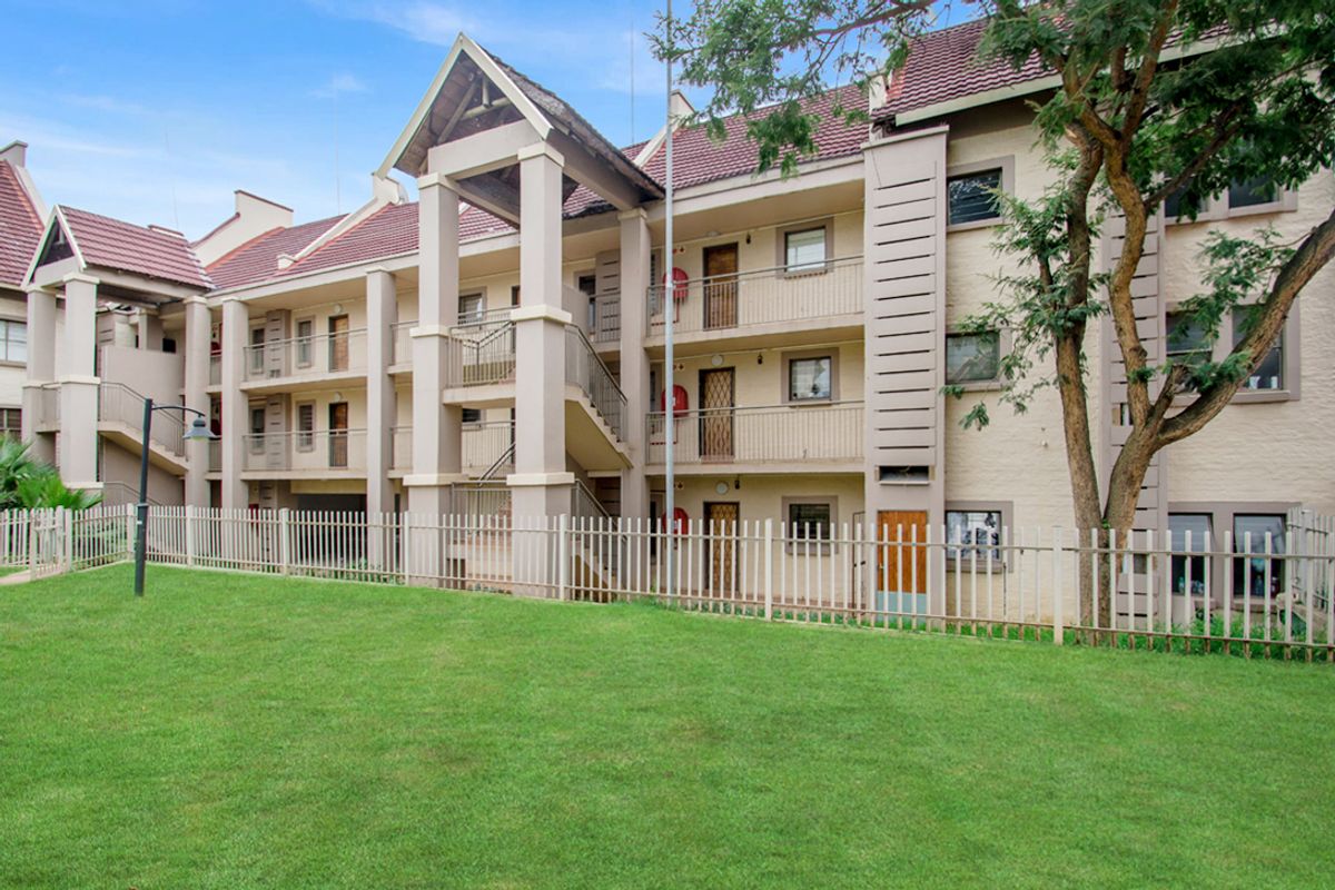 Exterior view of a multi-story apartment complex featuring a shared lawn, metal security fencing, and accessible balconies with external staircases.