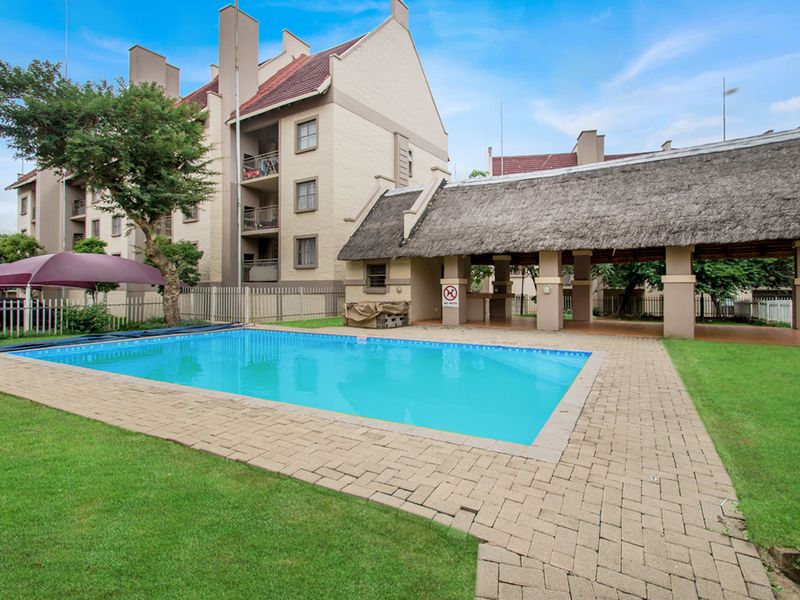 Communal swimming pool area featuring a paved deck and a covered thatched lapa with a built-in bar counter.