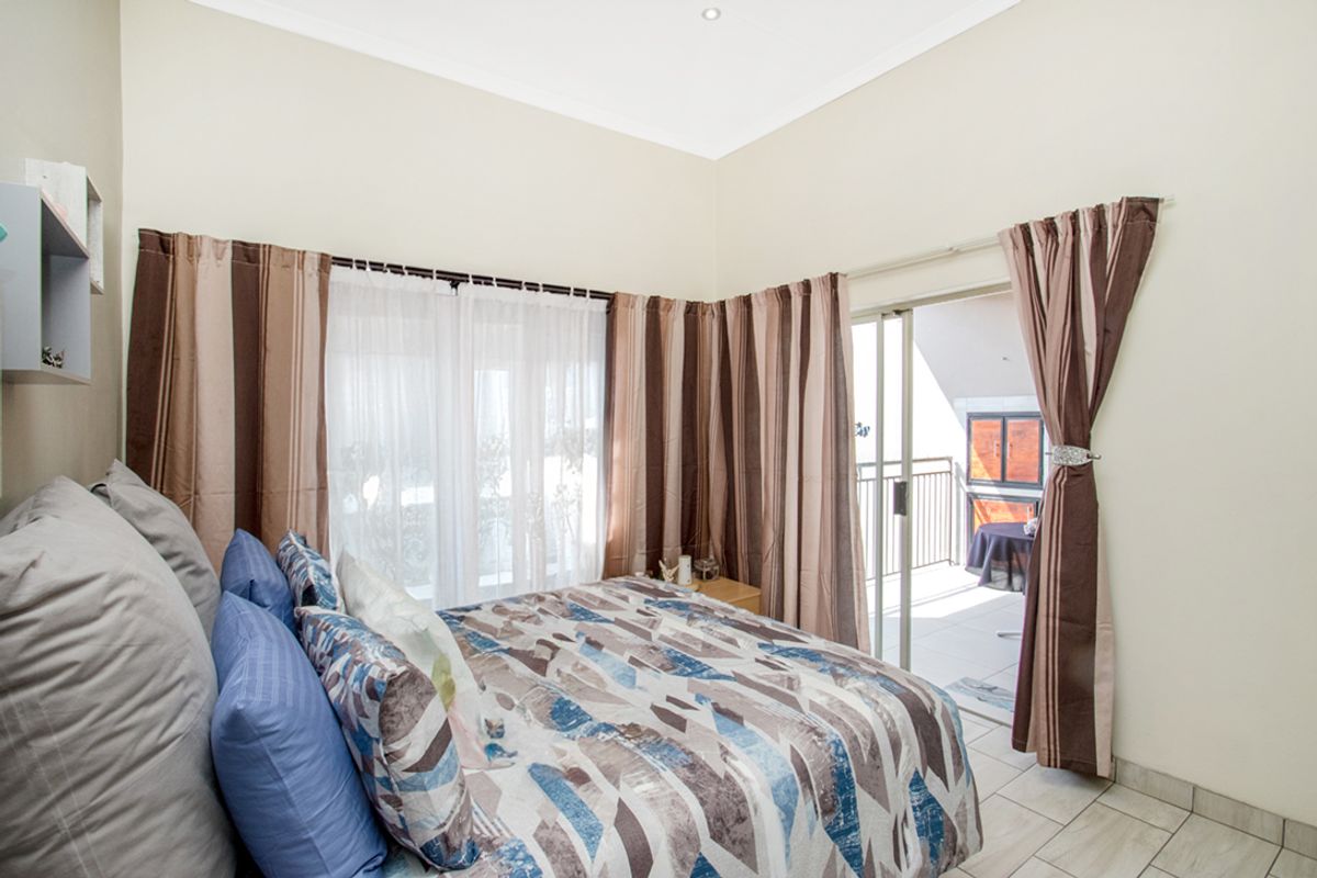 A well-lit bedroom featuring tiled flooring, recessed ceiling lights, and direct access to a private balcony through sliding glass doors.