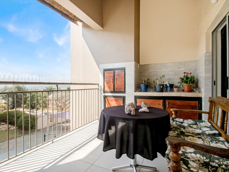 Covered balcony featuring a built-in braai, tiled flooring, and a metal balustrade with views of the surrounding area.