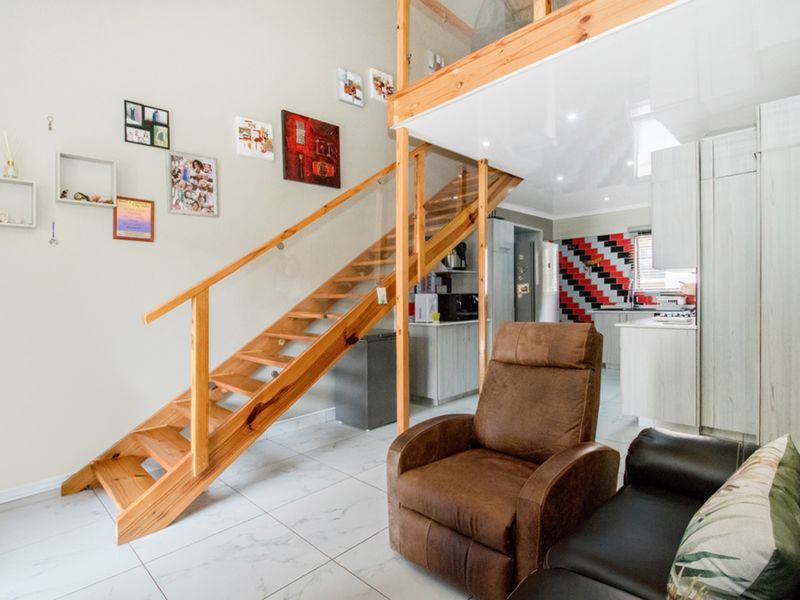 Open plan living area featuring a wooden staircase with glass balustrade leading to a mezzanine level, adjacent to a functional kitchen space.