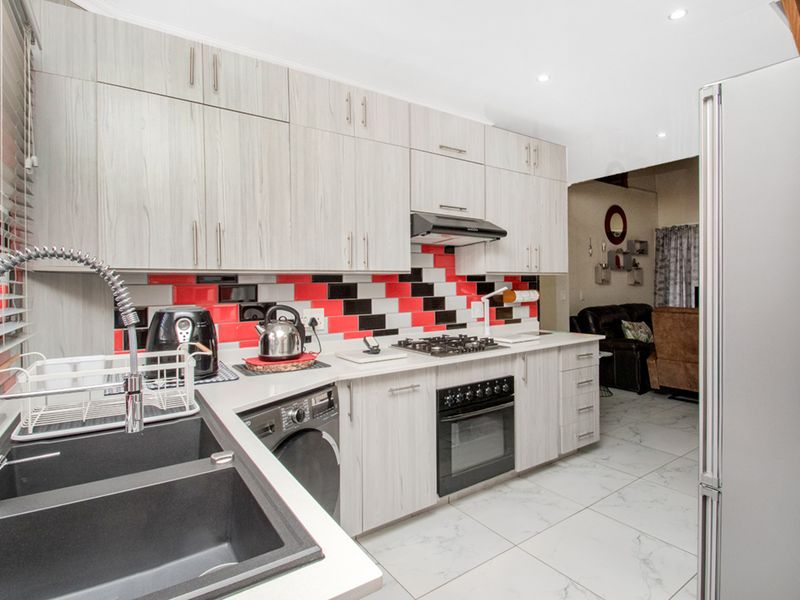 Modern kitchen featuring light wood-grain cabinetry, a striking red and black tiled backsplash, gas hob, built-in oven, and sleek tiled flooring.
