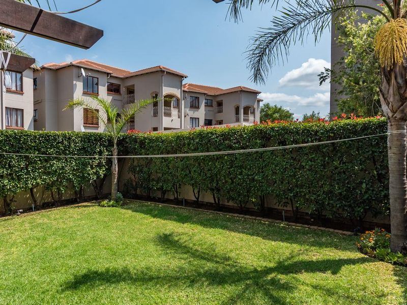 A well-maintained private garden featuring a manicured lawn, perimeter hedging, and a timber pergola structure, set against the backdrop of the townhouse complex.