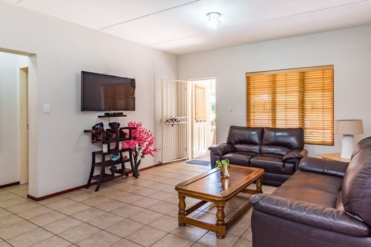 A living room featuring tiled flooring, a security gate at the entrance, and venetian blinds on the windows.