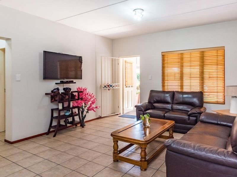 A living room featuring tiled flooring, a security gate at the entrance, and venetian blinds on the windows.