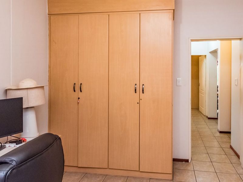A bedroom featuring light wood-finish built-in wardrobes, tiled flooring, and access to a hallway.