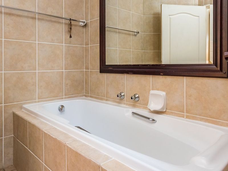 A functional bathroom featuring a built-in bathtub with wall-mounted fixtures, neutral ceramic wall tiling, and a large framed mirror.