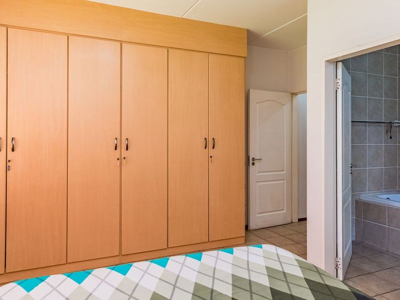 Bedroom featuring extensive built-in wooden cupboards and direct access to an en-suite bathroom with tiled finishes.