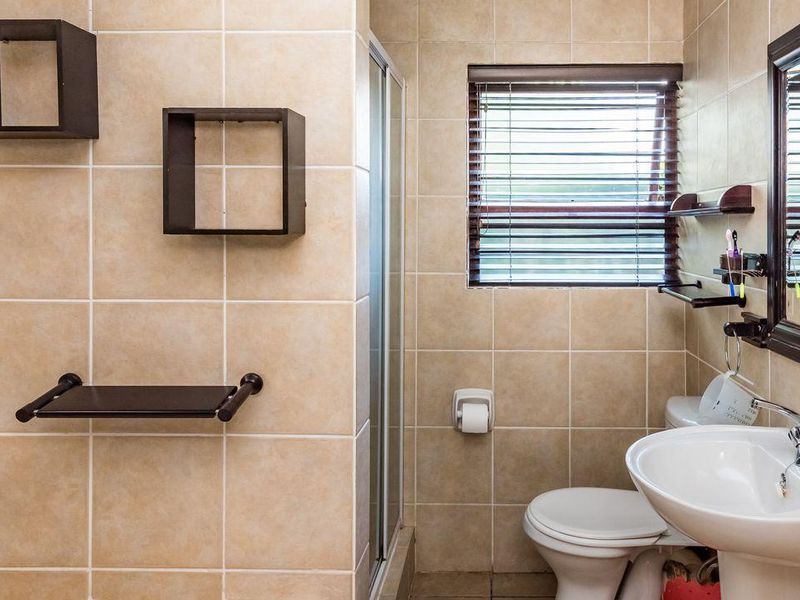 A functional bathroom featuring neutral ceramic wall and floor tiles, a pedestal basin, a toilet, and a glass-enclosed shower.