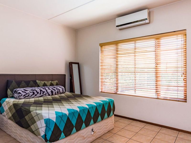 A well-maintained bedroom featuring tiled flooring, a wall-mounted split-system air conditioner, and timber venetian blinds for privacy.