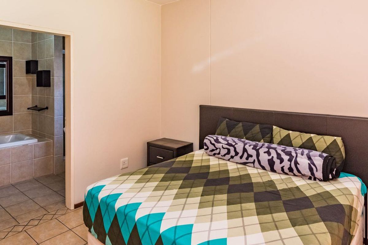 A bedroom featuring tiled flooring and an adjoining en-suite bathroom with a bathtub.