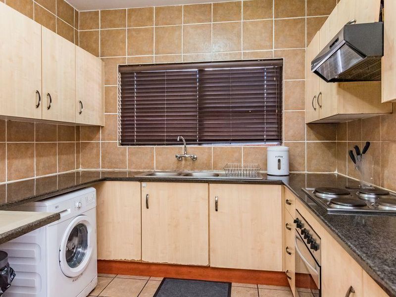 Functional kitchen featuring laminate cabinetry, granite countertops, built-in oven, electric hob, extractor fan, and tiled backsplash with integrated laundry plumbing.