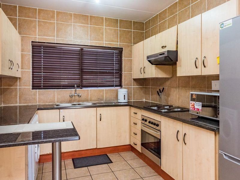 Functional kitchen featuring light wood cabinetry, granite countertops, built-in oven with hob, extractor fan, and tiled finishes throughout.