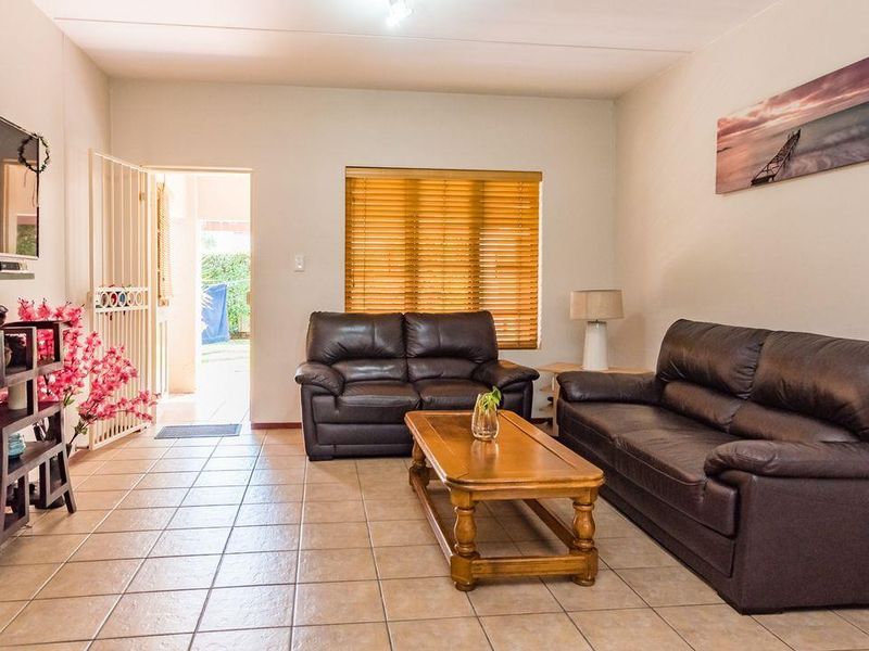 A comfortable living room featuring tiled flooring, a security gate leading to the exterior, and venetian blinds on the window.