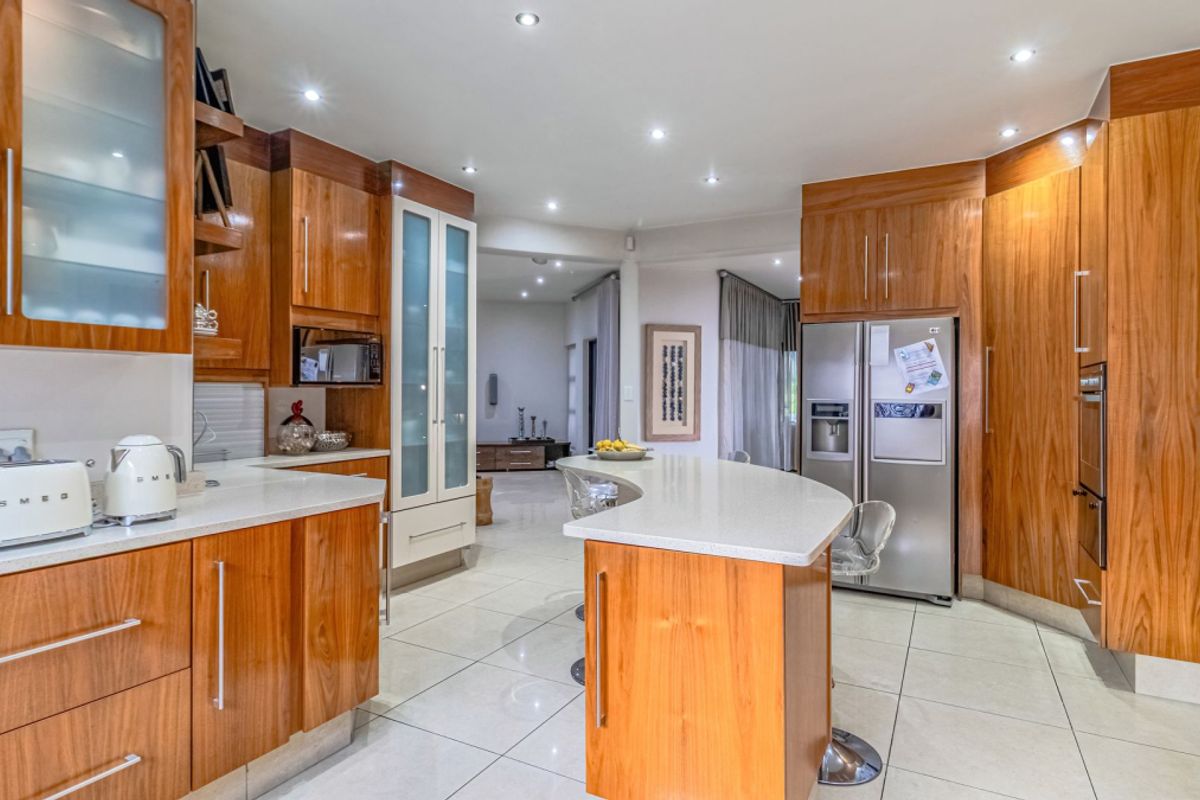 Modern kitchen featuring warm wood cabinetry, stone countertops, a central island, and integrated appliances, flowing into an open-plan living area.