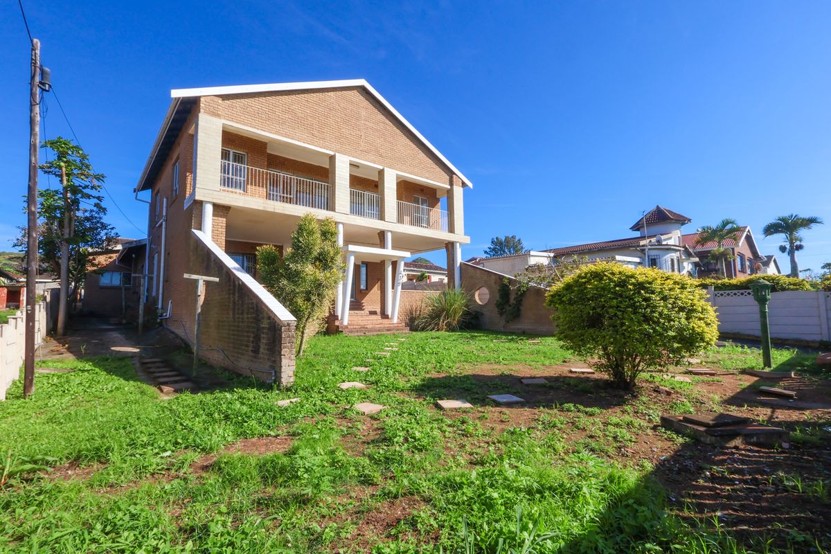 Rear view of a two-story brick house featuring a covered balcony with concrete pillars and a spacious garden area.