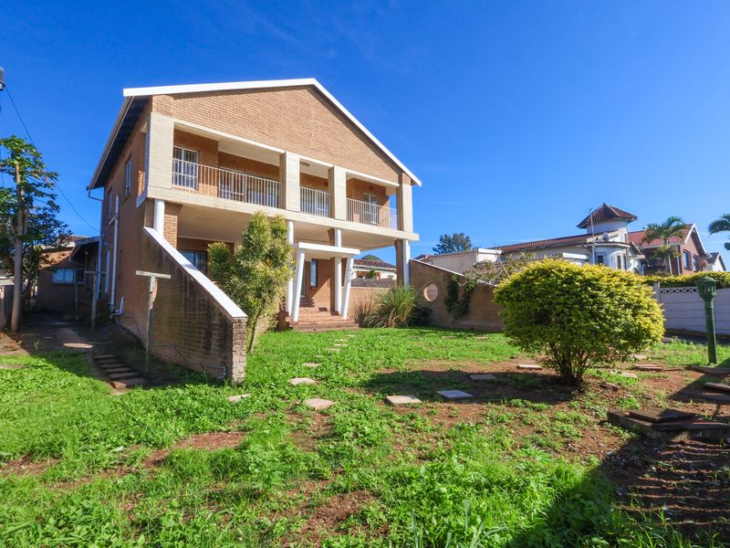 Rear view of a two-story brick house featuring a covered balcony with concrete pillars and a spacious garden area.