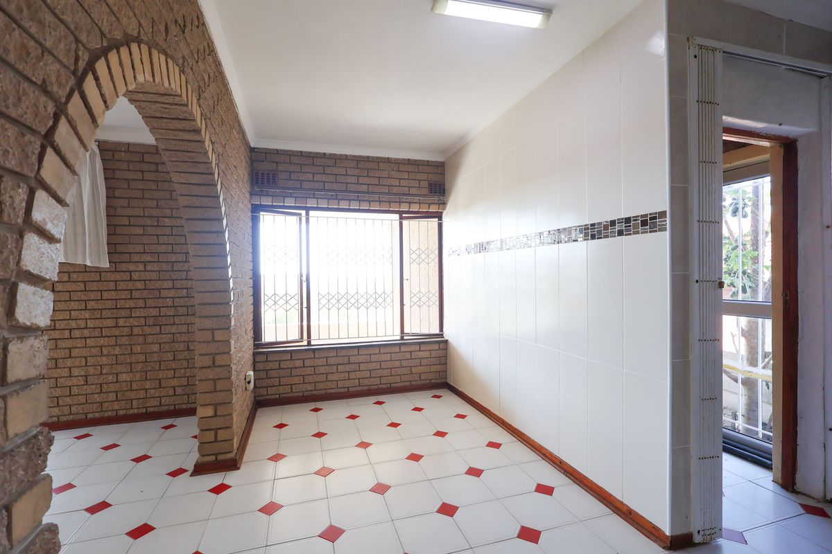 An empty kitchen area featuring a distinctive brick archway, tiled flooring with decorative accents, and a window with security bars.