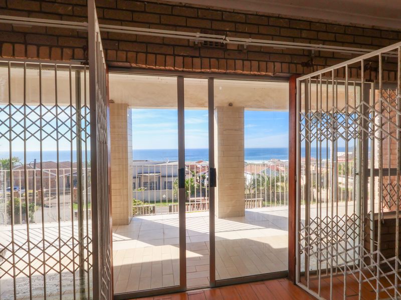 A covered balcony featuring tiled flooring and security gates, offering an expansive view of the surrounding neighborhood and the ocean.
