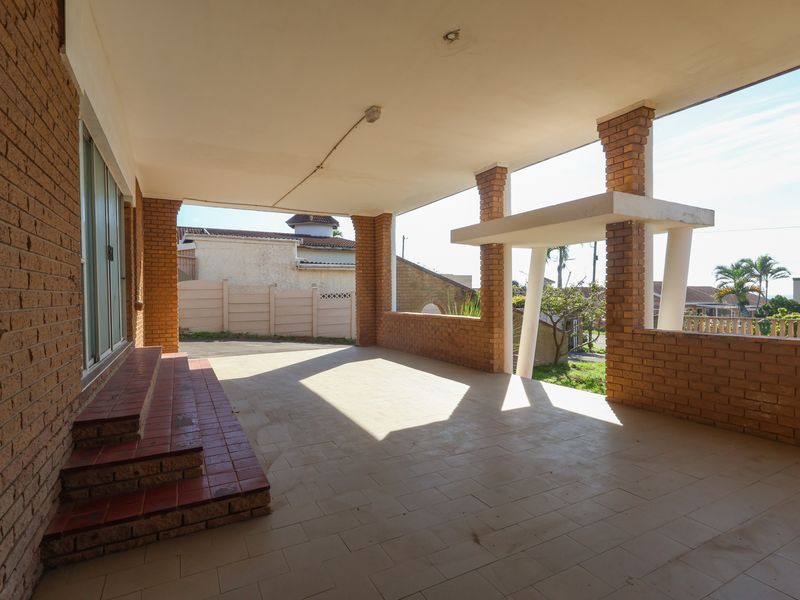 A spacious covered patio featuring brick pillars, tiled flooring, and direct access to the home through a sliding glass door.