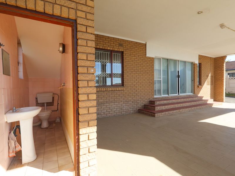 A covered patio area featuring brick exterior walls, sliding glass doors, and an adjacent outdoor toilet with a pedestal basin.