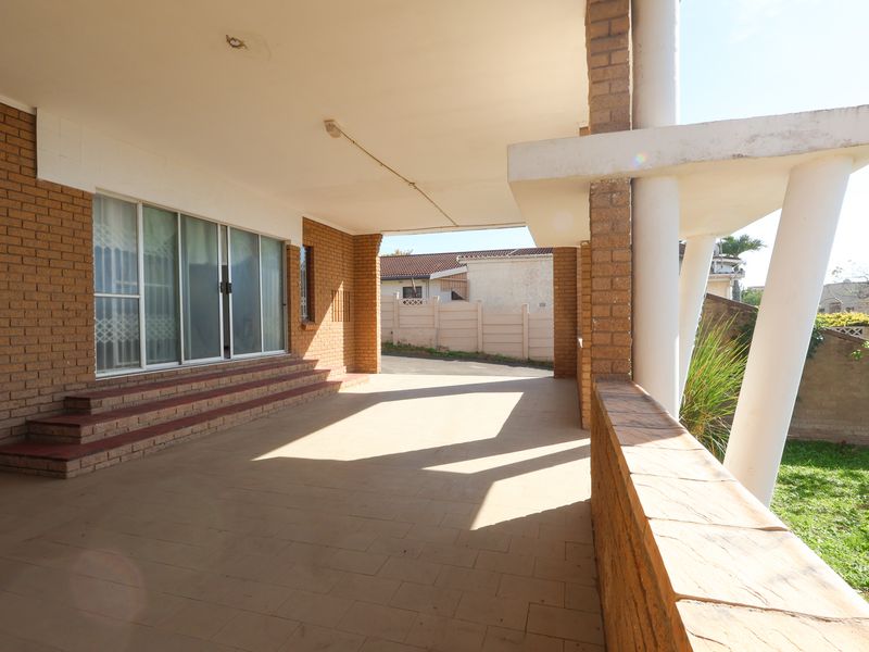A spacious covered patio featuring brick columns, tiled flooring, and direct access to the interior through sliding glass doors.