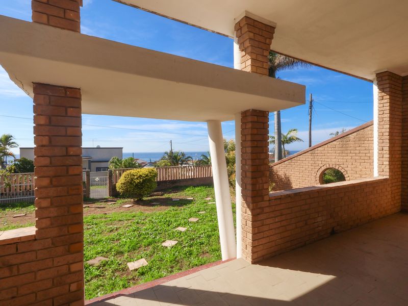 Covered patio area featuring exposed brick pillars and tiled flooring, overlooking a garden with distant sea views.