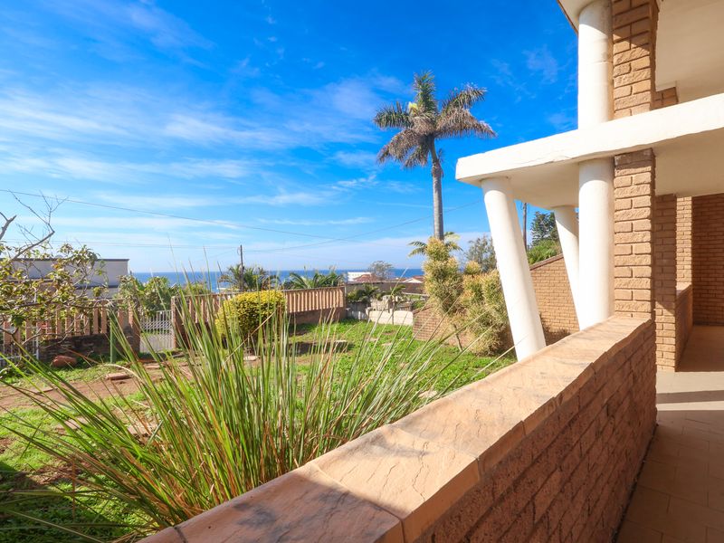 A covered patio area featuring brick columns and masonry walls, offering an open view of the garden and distant ocean horizon.