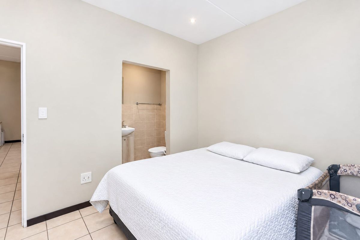 A bedroom featuring tiled flooring, neutral walls, and an integrated en-suite bathroom with a vanity basin and toilet.