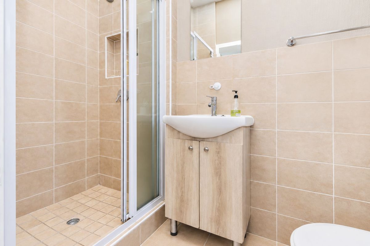 A clean, modern bathroom featuring a glass-enclosed shower, a wood-finish vanity cabinet with a basin, and neutral wall tiling.