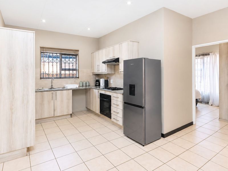 A functional kitchen featuring light wood-finish cabinetry, tiled flooring, built-in oven and hob, and a window with security bars.
