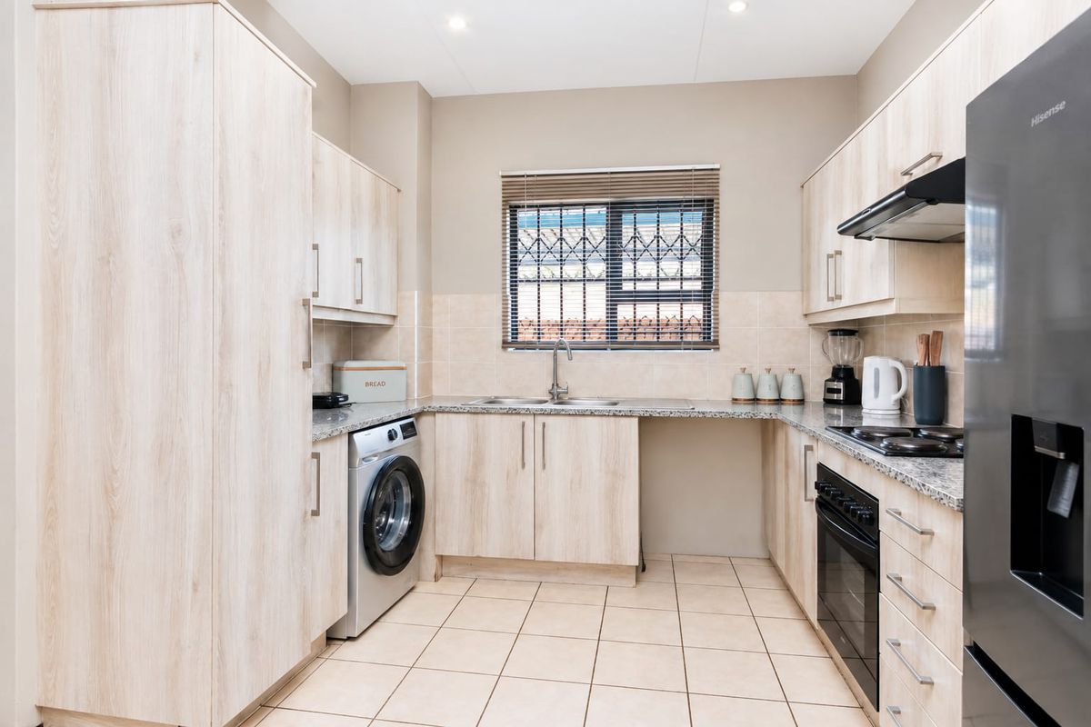 Modern kitchen featuring light wood-grain cabinetry, granite countertops, integrated oven and hob, and tiled flooring with a functional layout.