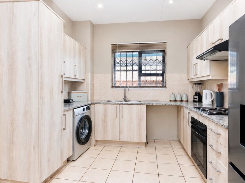 Modern kitchen featuring light wood-grain cabinetry, granite countertops, integrated oven and hob, and tiled flooring with a functional layout.