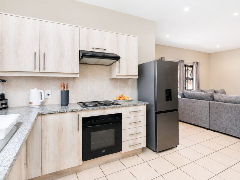 Modern open-plan kitchen featuring light wood cabinetry, granite countertops, built-in oven, and gas hob, seamlessly flowing into the adjacent living area.