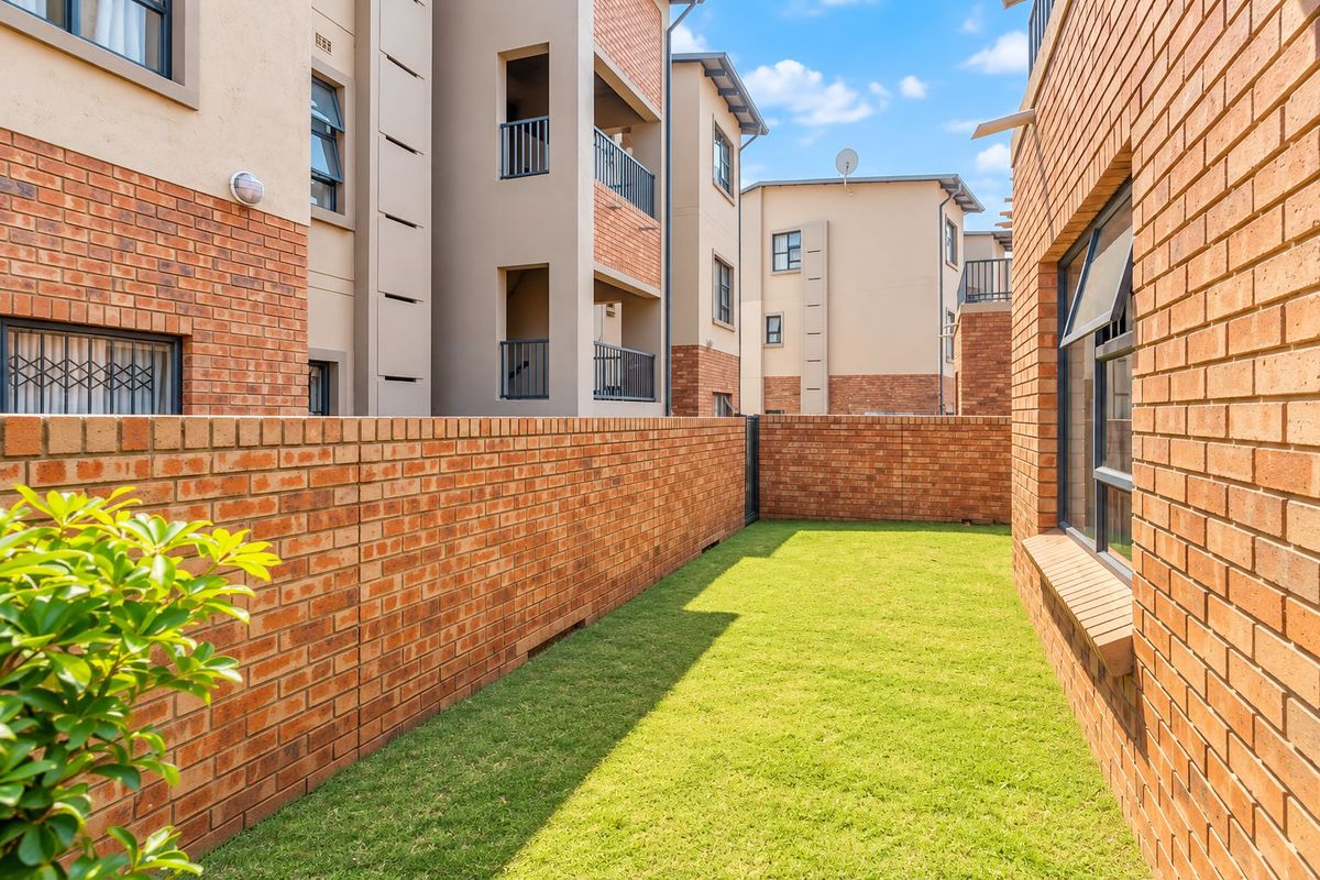 A private rear garden area featuring a well-maintained lawn enclosed by a face-brick boundary wall within an apartment complex.