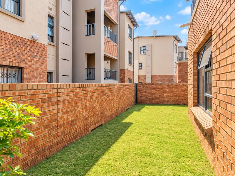 A private rear garden area featuring a well-maintained lawn enclosed by a face-brick boundary wall within an apartment complex.