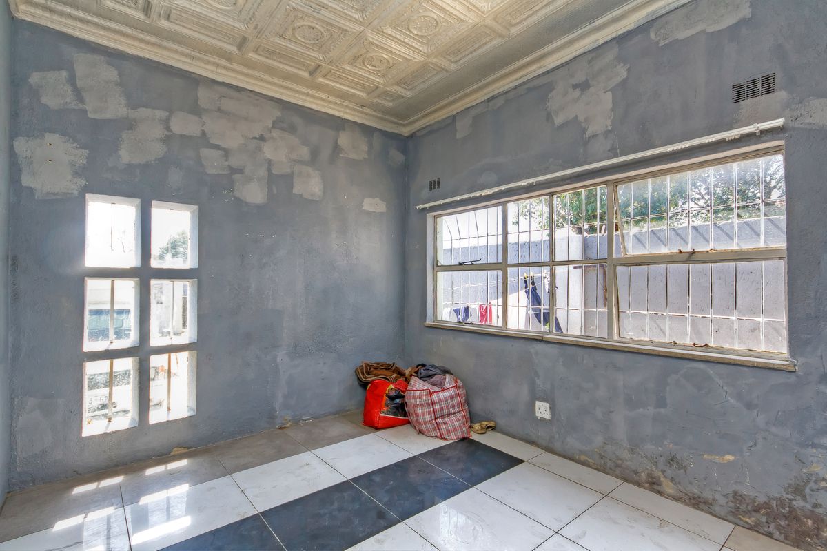 An empty living room featuring a decorative pressed metal ceiling, tiled flooring, and security bars on the windows, requiring cosmetic wall repairs.