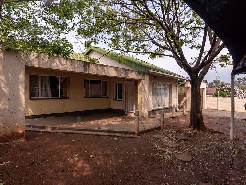 Front view of a single-story house featuring a covered patio, tiled roof, and a large tree in the front yard area.