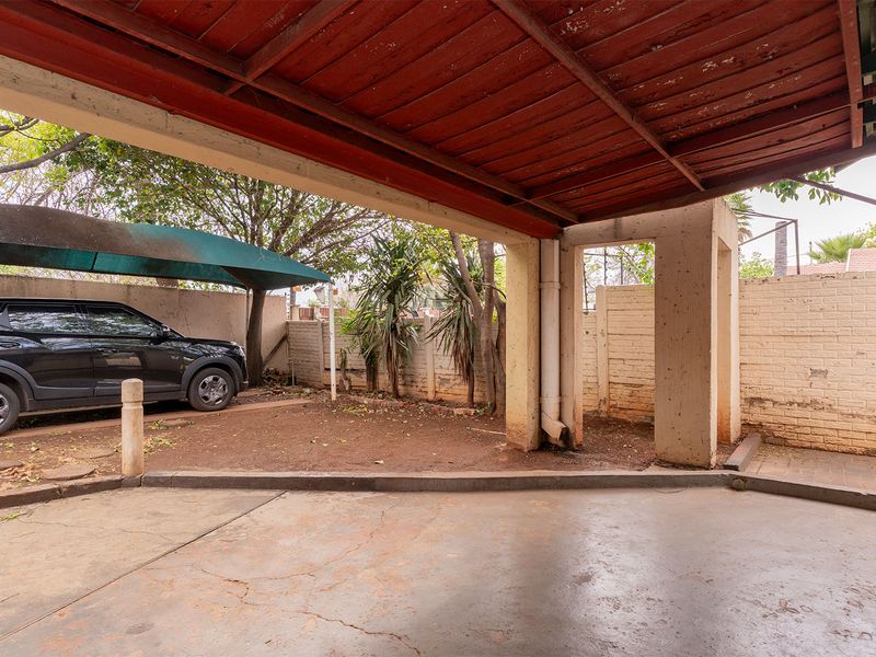 A covered outdoor patio area featuring concrete flooring and structural pillars, providing a functional space for vehicle parking or outdoor utility use.