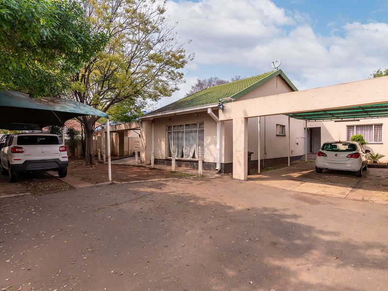 Front exterior view of the house featuring a paved driveway, multiple carports, and a tiled roof structure.