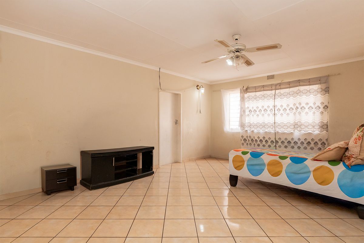 A spacious bedroom featuring neutral tiled flooring, a ceiling fan, and coved cornicing, offering a blank canvas for potential interior updates.