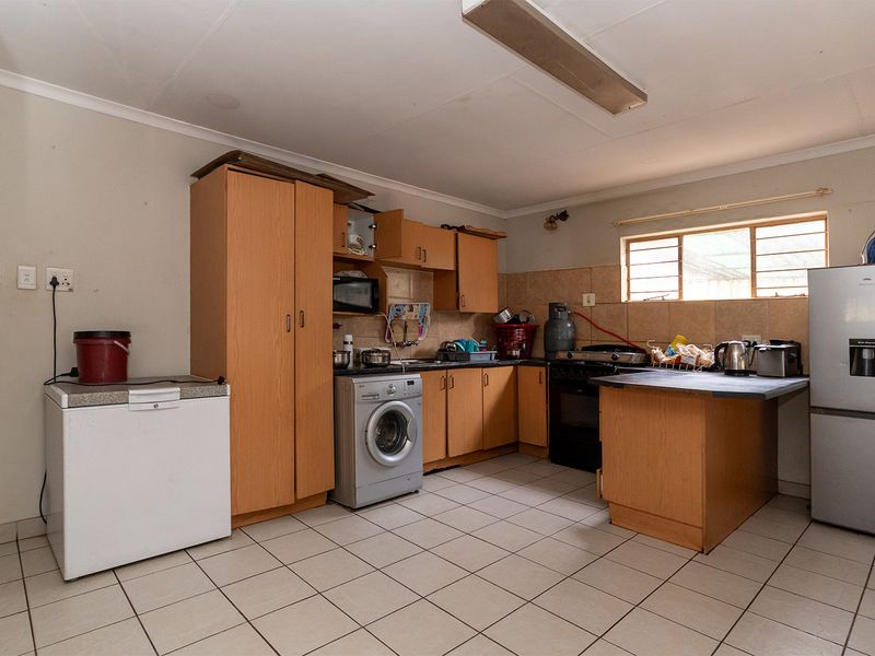 A functional kitchen featuring built-in wooden cabinetry, tiled flooring, and a tiled backsplash, offering a practical layout with integrated appliance connections.