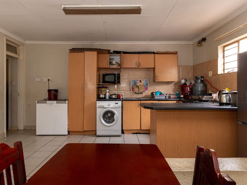 A functional kitchen featuring built-in wooden cabinetry, tiled backsplash, and a breakfast bar, offering a practical layout with tiled flooring throughout.