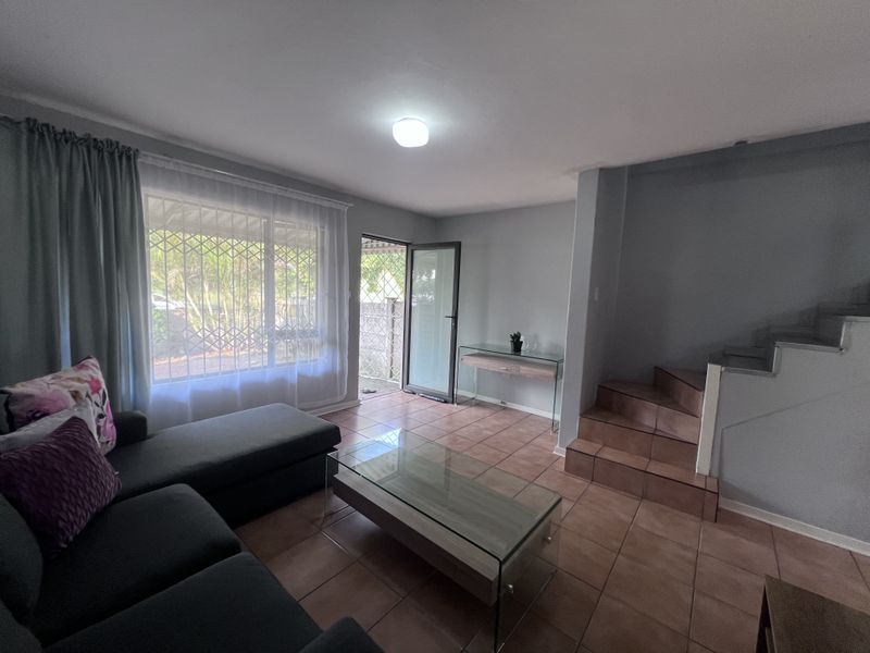 A living room featuring tiled flooring, a staircase, and access to an outdoor area through a sliding door with security bars.