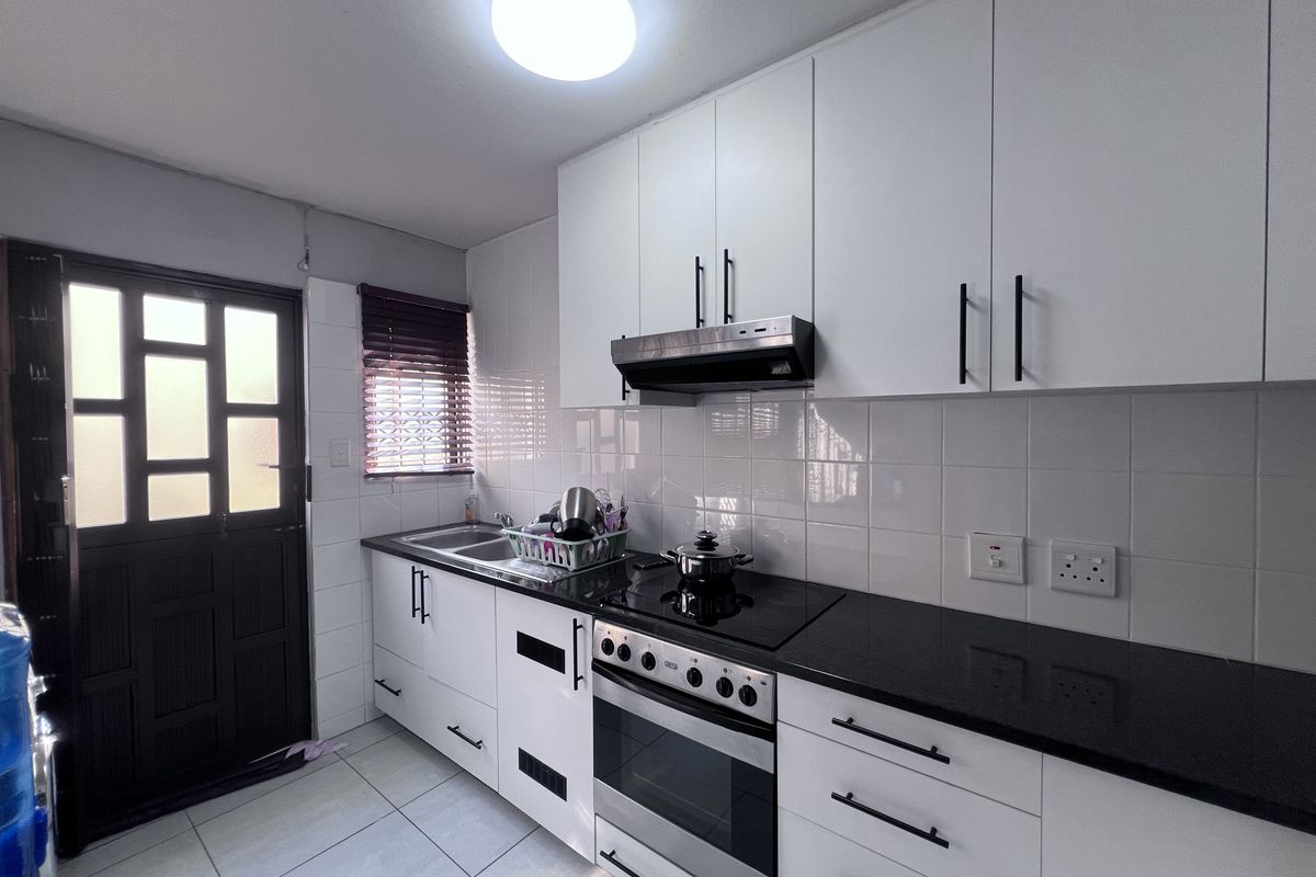 Modern kitchen featuring white cabinetry, black granite countertops, integrated oven and hob, tiled backsplash, and direct access to an external door.