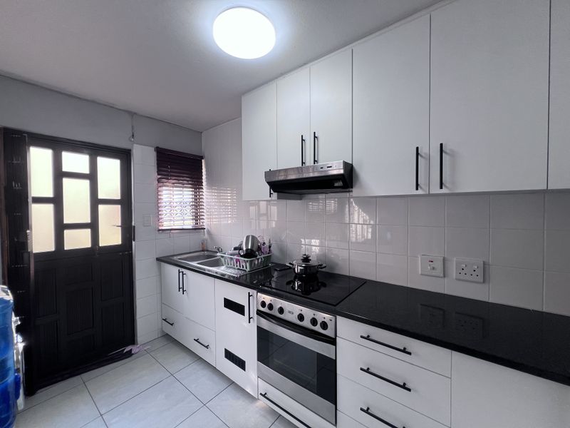 Modern kitchen featuring white cabinetry, black granite countertops, integrated oven and hob, tiled backsplash, and direct access to an external door.