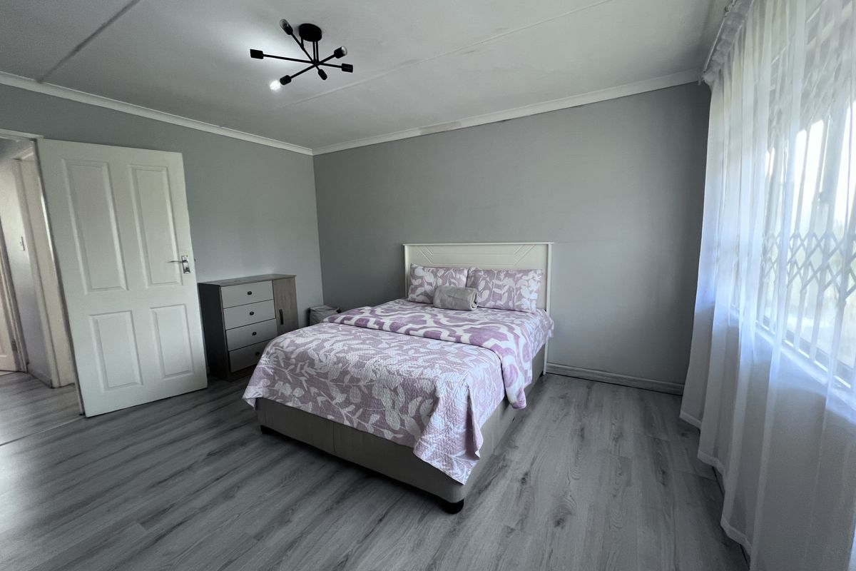 A well-maintained bedroom featuring modern grey laminate flooring, neutral wall tones, and a security gate on the window.