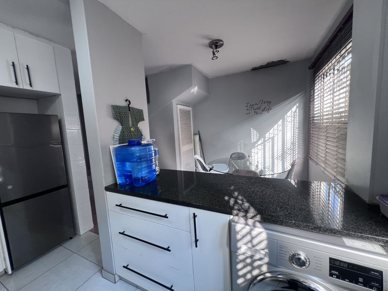 Kitchen area featuring granite countertops, white cabinetry, and an integrated washing machine, with visible ceiling damage requiring repair.