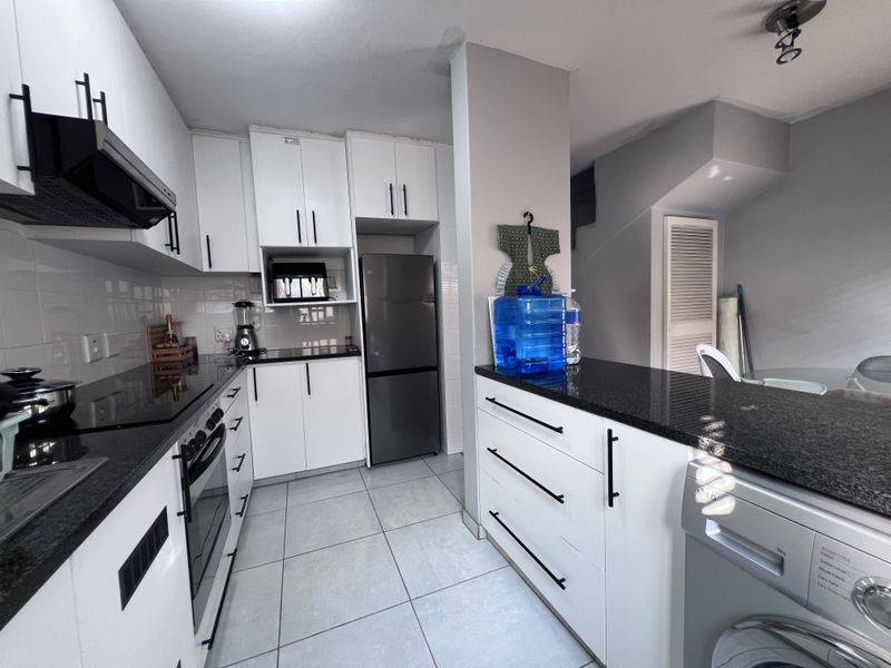 Modern kitchen featuring white cabinetry, black granite countertops, built-in oven and hob, and tiled flooring with an integrated laundry area.