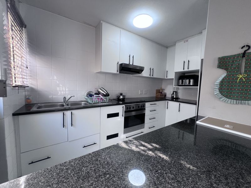 Modern kitchen featuring white cabinetry, dark granite countertops, a built-in oven with extractor fan, and a functional breakfast bar area.